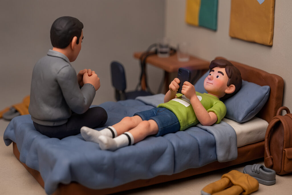 Un père parle assis sur le lit de son fils ado. L'ado a son téléphone en mains mais regarde le père. Scène en pâte à modeler.