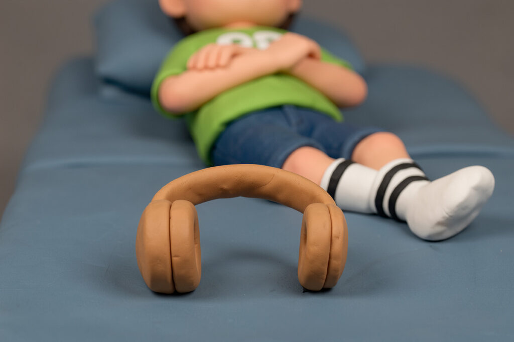 Un casque sans fil posé sur un lit d'adolescent, le garçon y est couché. Pas de visage visible. Scène en pâte à modeler.