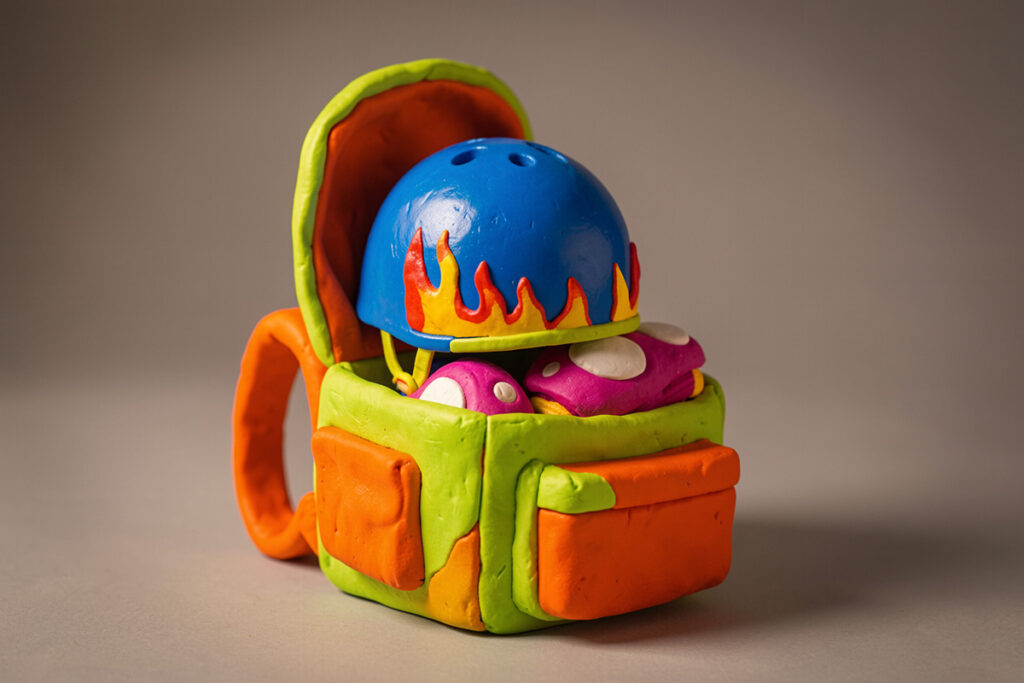 Un sac à dos coloré contenant un casque de skateboard coloré et des genouillères colorées. Pâte à modeler.